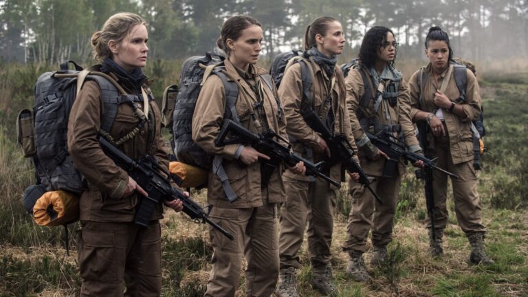 Five women in tan field gear with large backpacks and rifles stand in a misty wooded clearing.
