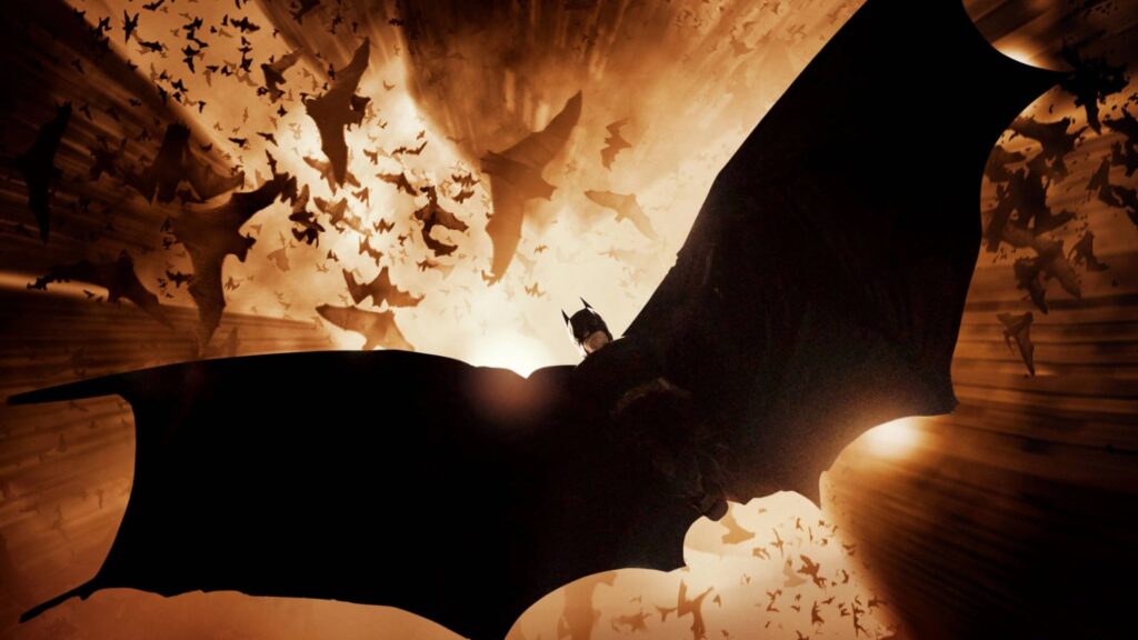 Sepia-toned cinematic illustration of a black-caped, pointed-eared masked figure silhouetted against a bright burst of light, surrounded by flying bats.