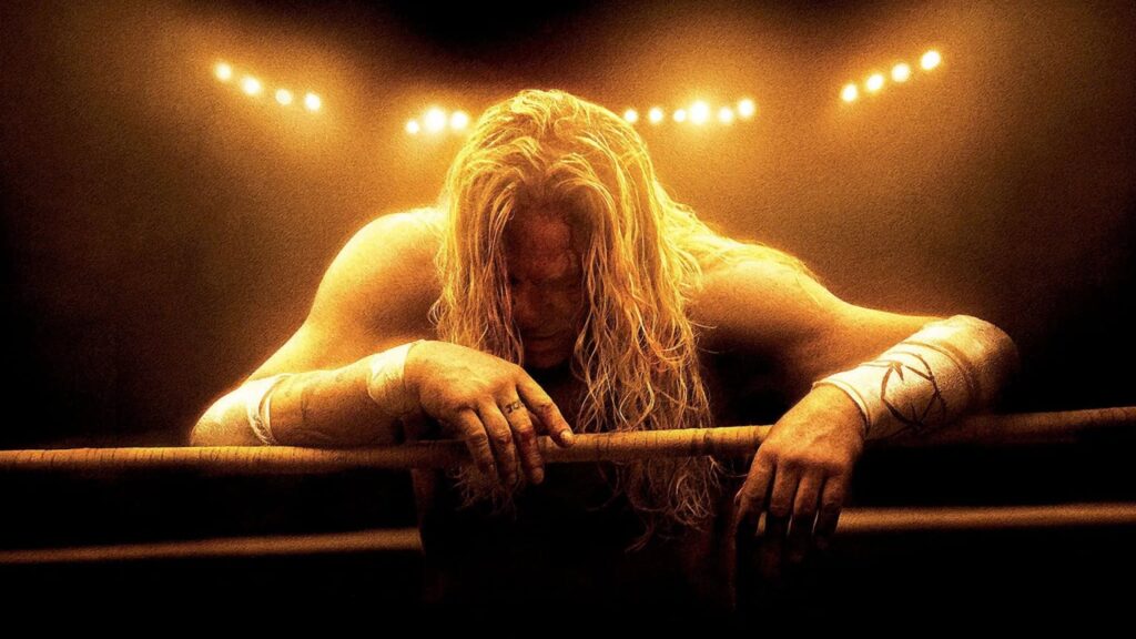 A long-haired, muscular wrestler slumps over ring ropes beneath warm arena lights, with taped wrists and head bowed in exhaustion.